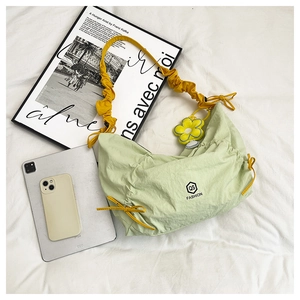 Detail of green nylon crescent bag featuring yellow drawstrings and flower charm