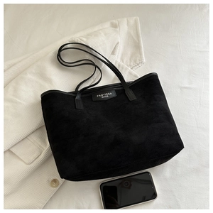 Detail of black suede tote bag with brand label shown next to a smartphone for scale