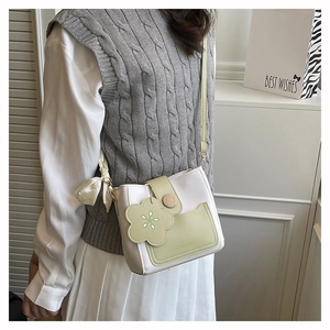 Detail of crossbody bucket bag featuring floral charm and white satin ribbon bow
