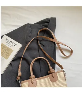 Detail of woven straw handbag with brown leather handles and adjustable long shoulder strap