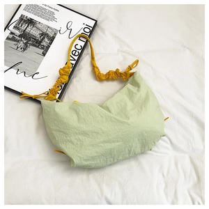 Detail of green crescent bag with yellow ruched strap and nylon texture on white fabric