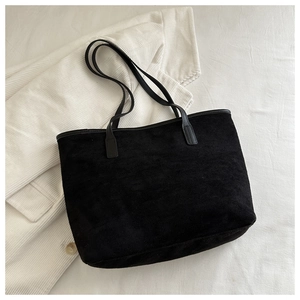 Detailed top view of a black suede tote bag with matte texture on a white corduroy coat
