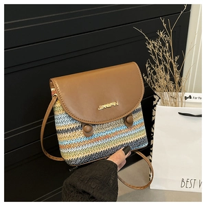 Détail du sac seau bandoulière en paille rayée avec rabat en cuir brun et logo métallique