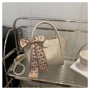 Close-up of cream bucket bag with lychee texture and decorative silk scarf on silver shelf
