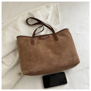 Detailed close-up of brown suede tote bag texture with brand logo and smartphone for scale