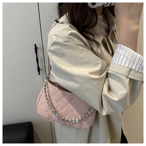 Détail du sac baguette rose matelassé avec chaîne de perles et broderie fleurie sur manteau