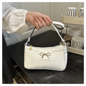 Dettaglio della borsa in vernice bianca con fiocco dorato e ciondolo a forma di fiore