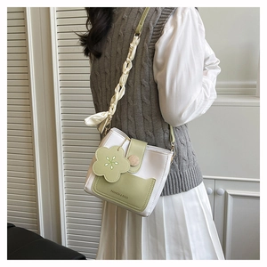 Detail of trendy mini crossbody bag featuring a green flower charm and ribbon handle wrap
