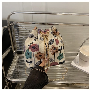 Détail du sac seau tissé avec motifs floraux, chaîne dorée et cordons en perles