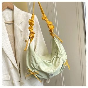 Detail of light green crescent nylon bag featuring yellow pleated straps and bow decor