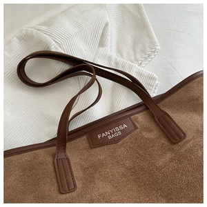 Detail of FANYISSA brown suede tote bag featuring leather logo plaque and stitched straps