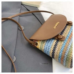 Detail of colorful striped straw bucket bag with brown leather flap and metal logo