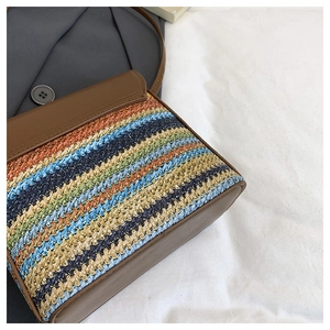 Detail showing colorful woven straw texture and brown leather stitching on shoulder bag