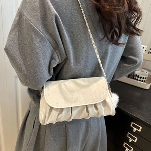 Détail du sac bandoulière plissé crème avec pompon en peluche et logo gravé