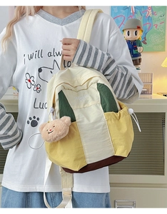 Side view of multi-color nylon backpack with contrast panels and plush bear charm