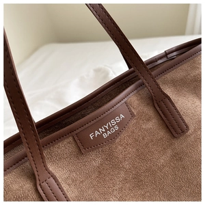 Close-up of brown suede tote bag featuring reinforced leather handles and logo patch