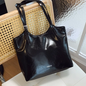 Glossy black leather tote bag with FASHION text hanging on a stylish wooden chair