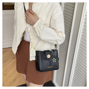 Detail of black leather crossbody bucket bag with gold button and floral charm pendant