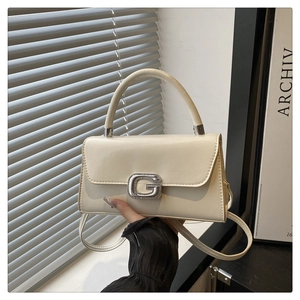 Detail of a creamy white crossbody bag featuring a sparkling crystal G-shaped metal buckle