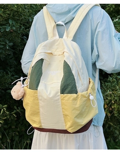 Detail of color-block nylon backpack featuring side drawstring pocket and plush bear charm
