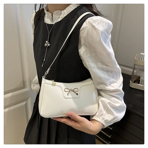 Dettaglio borsa bianca in pelle lucida con fiocco dorato e ciondolo zip a fiore