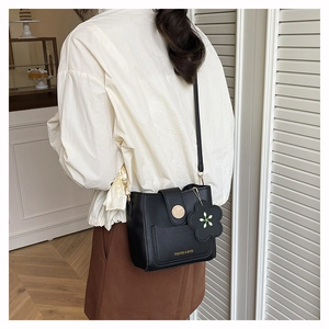 Detail of black leather bucket bag with gold magnetic clasp and floral charm on the side