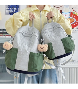 Detail of color-block nylon backpack featuring plush bear charm and brand embroidery