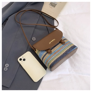 Détail du sac bandoulière en paille rayé avec rabat en cuir sur literie blanche