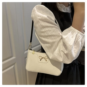 Elegante borsa baguette in pelle verniciata bianca con fiocco dorato indossata