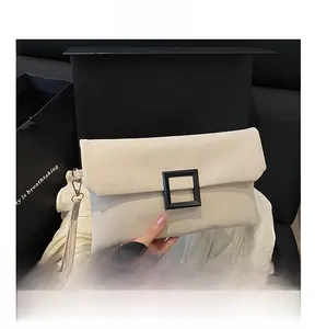 Detail showing beige leather envelope bag with matte black square buckle on white silk