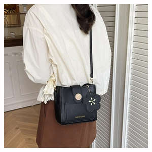 Détail du sac bandoulière noir en PU avec breloque fleur et logo doré sur le modèle