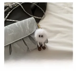 Close-up of grey pleated shoulder bag featuring a cute plush cartoon charm with chain strap
