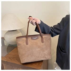 Macro detail of brown suede tote bag featuring reinforced leather edges and logo patch