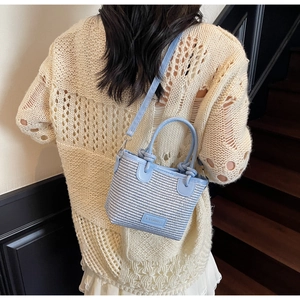 Crossbody view of light blue woven bucket bag with knotted handle and FASHION tag