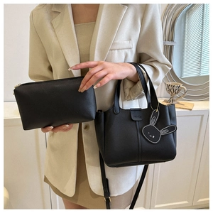 Detail view of black litchi pattern crossbody bag with fashion rabbit pendant on beige suit