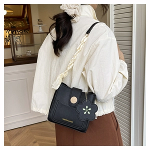 Detail of black bucket bag with gold lettering, silk-wrapped strap, and floral charm
