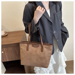 Brown faux suede tote bag with minimalist logo patch shown on a model's shoulder