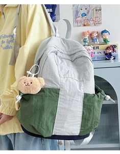 Detail view of water-resistant nylon backpack with side drawstring pocket and plush bear charm