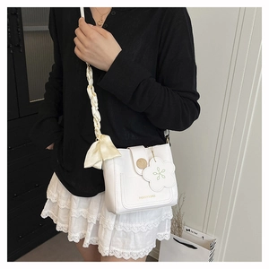Detail of white bucket bag with floral charm, silk scarf strap and gold twist lock