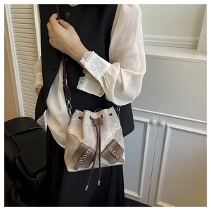 Detail of grey bucket bag with drawstring closure and brown leather trim on a model