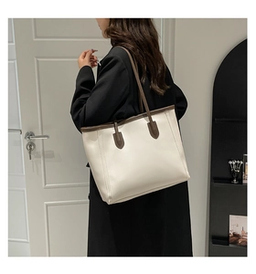 Model wearing a minimalist cream tote bag with brown straps in a modern interior setting
