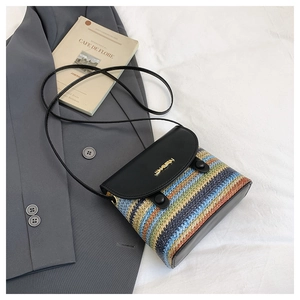 Détail du sac seau en paille rayé avec rabat en cuir noir et logo doré brillant