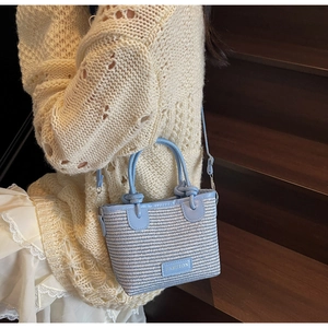 Detail of blue and white woven straw bag featuring fashion label and faux leather strap