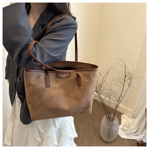 Brown suede tote bag side view with long handles worn over a grey blazer and skirt