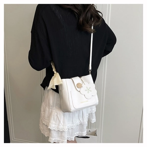 White bucket bag with flower charm and silk scarf strap shown on shoulder