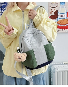 Detail of color-block nylon backpack featuring plush bear pendant and side drawstring pockets