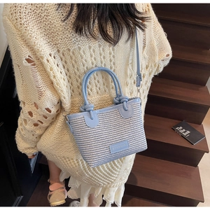 Close-up of a blue and white woven crossbody bag with round handles on wooden stairs
