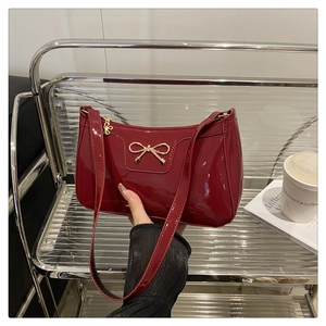 Dettaglio della borsa baguette in vernice rosso scuro con fibbia a fiocco dorata