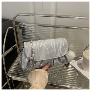 Détail d'un sac bandoulière en satin plissé argenté avec chaîne et pompon blanc
