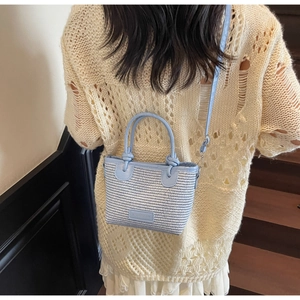 Detail of light blue woven crossbody bag with adjustable strap and top handles